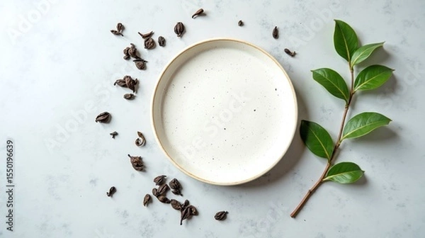 Obraz The image features a white plate with speckled design surrounded by small, dark seeds and a green leafy sprig against a light, textured background.