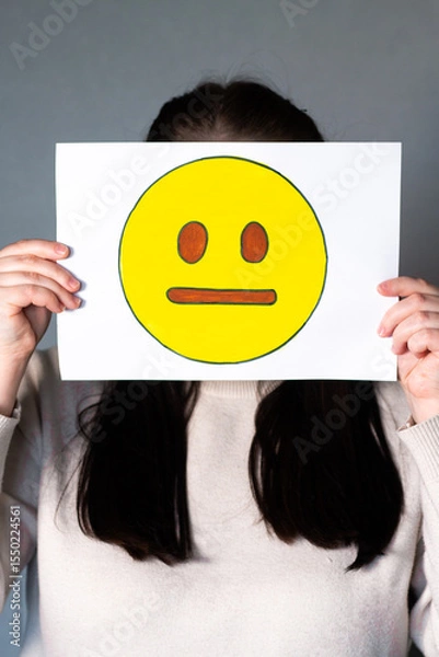 Fototapeta Woman holding emoji mask without smile and any expression in front of face. Social media trends, Gen Z marketing, World emoji day 17 July.