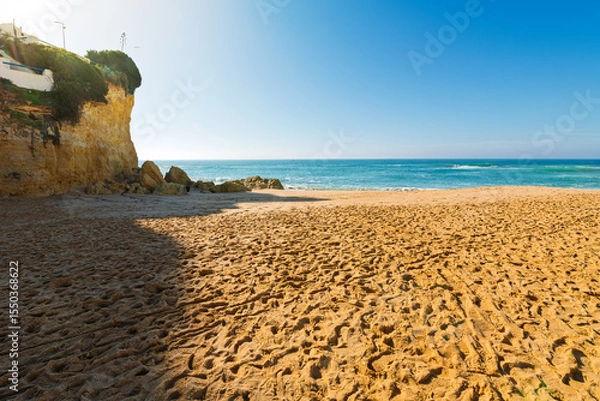 Fototapeta The sandy Praia de Carveiro Beach with the cliffs and hillside village of Carvoeiro, Portual in view along the Algarve coast of Southern Portugal.	