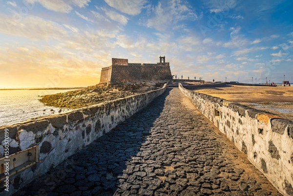 Fototapeta Sunset view of the Castillo de San Gabriel or Castle of San Gabriel, a 16th century fortress extending into the bay of Arrecife, in Arrecife Spain on the Canary island of Lanzarote.	