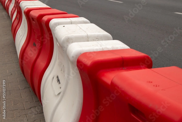 Obraz Red and white plastic road barriers used for traffic control and construction site safety. Urban street infrastructure element close-up
