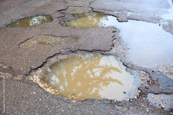Fototapeta Wet potholes on asphalt road with reflections from rainwater