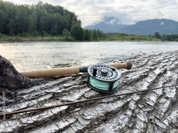 Fototapeta Fishing fly reel and pole resting on log with Skagit river and mountains in background