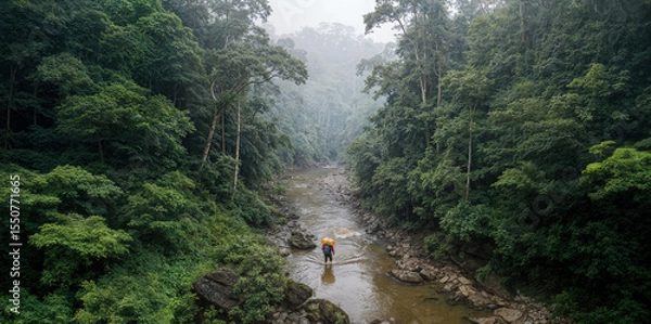 Obraz Aerial view captures a smuggler with a large contraband backpack attempting to cross a remote, misty jungle river. Concept of illegal border crossing, crime, illicit trade, remote location, danger. 