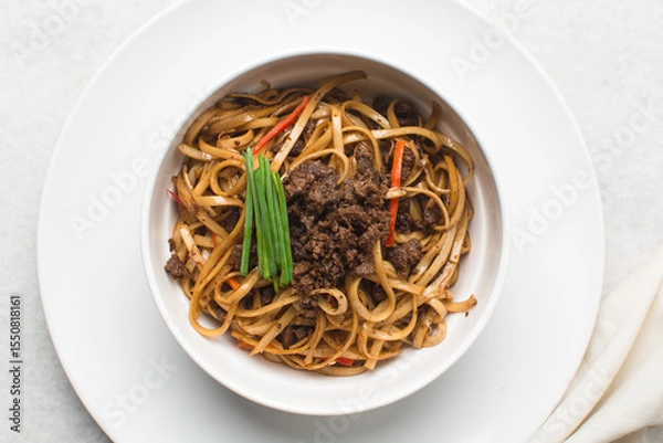 Obraz Overhead view of mongolian ground beef noodles in  a white bowl, top view of ground beef noodles with green and red pepper