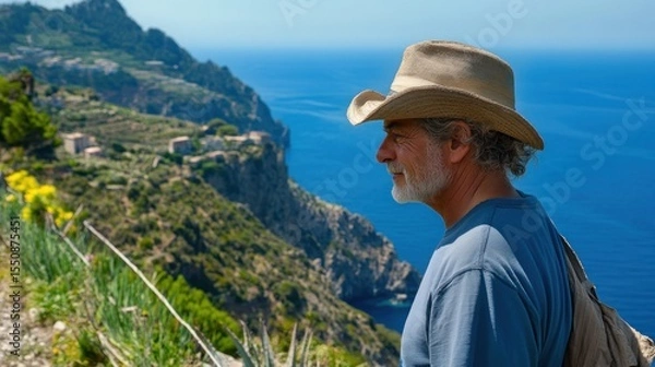 Obraz Mature man in cowboy hat enjoys scenic coastal view from a hillside.