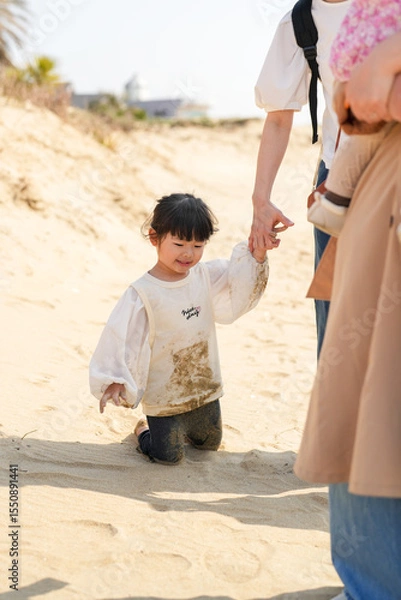 Fototapeta In early March, Japanese families enjoy the beach together: a 6-month-old baby, a 1-year-old girl, a 3-year-old girl, and parents in their 30s. A cheerful springtime scene filled with warmth and joy.