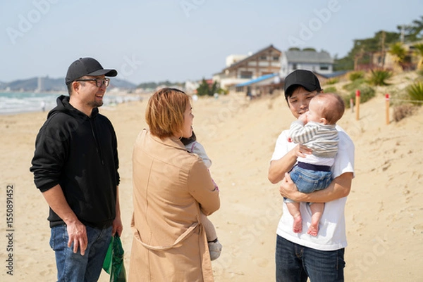 Fototapeta In early March, Japanese families enjoy the beach together: a 6-month-old baby, a 1-year-old girl, a 3-year-old girl, and parents in their 30s. A cheerful springtime scene filled with warmth and joy.