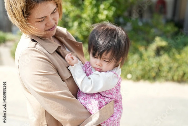 Fototapeta In early March, a Japanese mother in her 30s holds her 1-year-old daughter on a sandy beach by the sea. A heartwarming springtime moment filled with warmth and tenderness along the quiet shoreline.