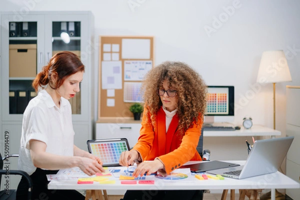 Fototapeta Two female designers brainstorming color palettes in a modern office. Creative teamwork, branding, and UI UX