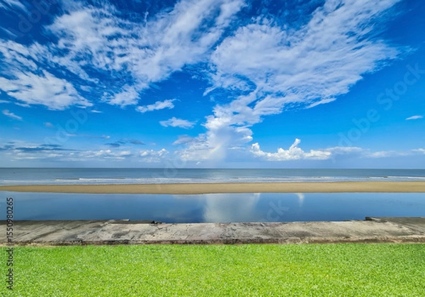 Fototapeta Tropical Beach View with Blue Sky, Clouds, and Green Grass Foreground