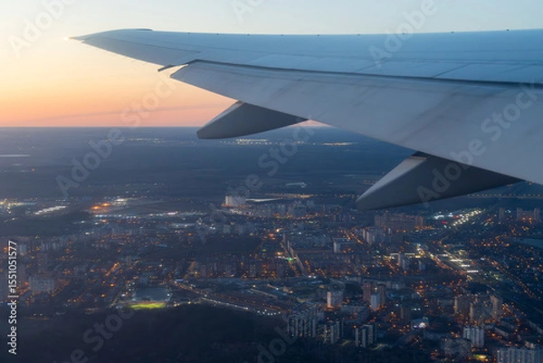 Fototapeta View from an airplane of the city and its surroundings. Beautiful evening aerial landscape. Buildings and streets under the wing of an airplane. Flying on an airplane. Travel and aviation tourism.
