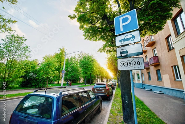 Fototapeta Parked cars under leafy trees in residential area, paid parking zone sign on pole, issue of limited free parking spaces. Roadside view in green residential zone with vehicles parked closely under tree