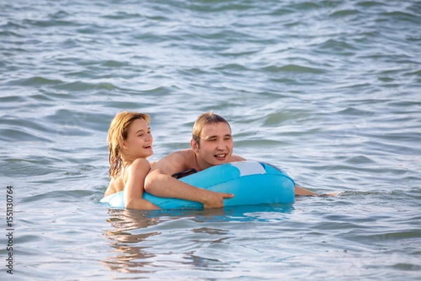 Fototapeta A cheerful young couple swims in the sea with an inflatable circle