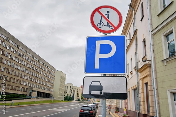 Fototapeta Pole in downtown street displays signage for traffic and pedestrian rules including no scooter zone and specific parking regulations. Pole with regulatory signs, no scooter riding, parking lot symbols