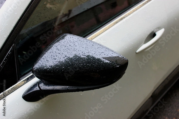 Obraz The black side mirror of a white car is covered with large raindrops