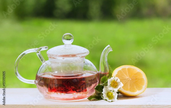 Fototapeta Teapot with fragrant herbal tea on a background of nature lemon and strawberry flower
