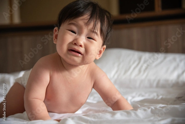 Fototapeta A crying Asian baby on the bed of six months has woken up and is calling for her mother