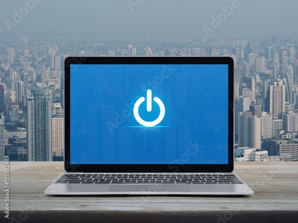Fototapeta Power button flat icon on modern laptop computer screen on wooden table over city tower and skyscraper, Start up business online concept