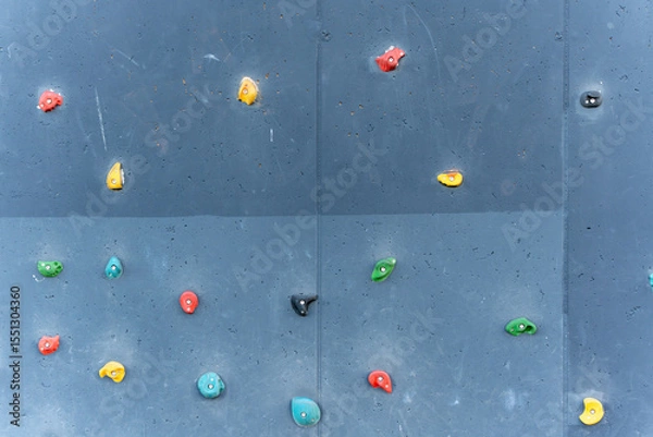 Fototapeta A vertical climbing wall with colorful holds against a gray background. The various shapes and colors offer a playful, challenging design for sport or playground use.