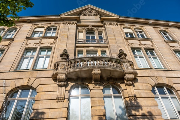 Fototapeta A magnificent old building with a detailed facade, high windows, and a circular balcony in the center. The Baroque elements and the blue sky emphasize the classical style.