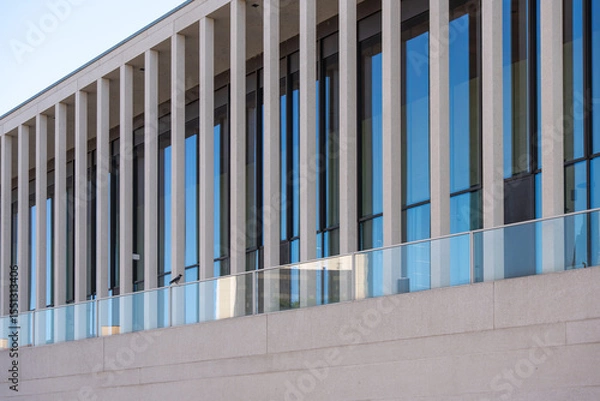 Fototapeta A modern building with vertical concrete struts and a continuous glass front. The clean lines and reflections create a minimalist aesthetic.