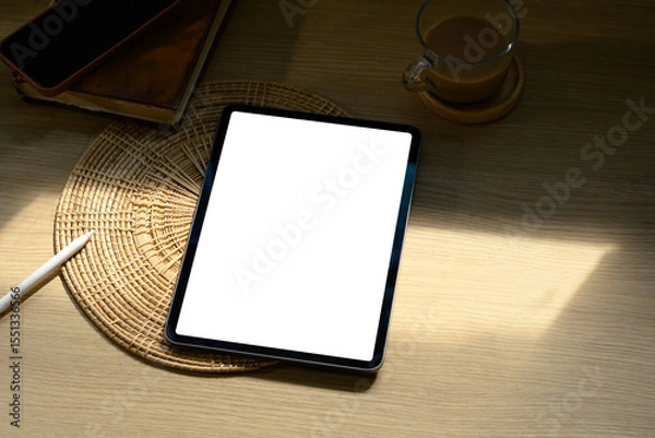 Fototapeta Digital tablet with blank screen on wooden desk beside coffee cup in soft morning light