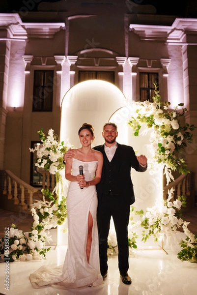 Fototapeta a bride and groom in front of a wedding arch decorated with flowers