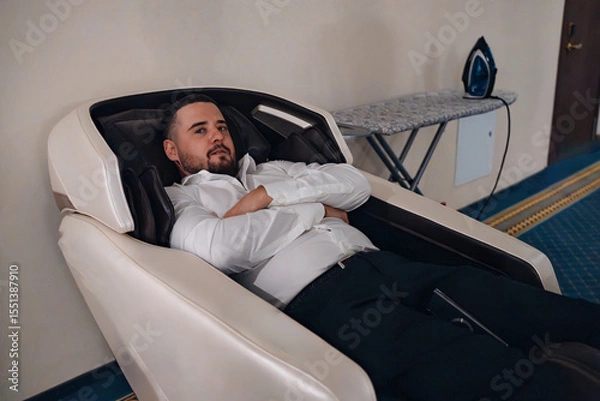 Obraz A brunette man with a beard lies in a massage chair in the corridor of the hotel