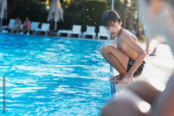 Fototapeta Caucasian boy sitting on the edge of the pool after swimming, summer holidays and travel concept