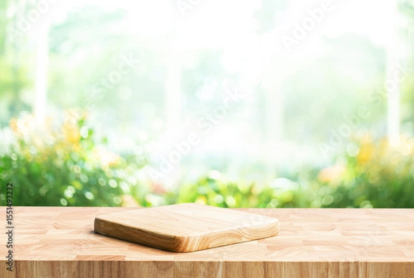 Fototapeta Cutting board placed on a textured wooden countertop, with soft sunlight streaming through house wall area  and blurred green landscape in the background