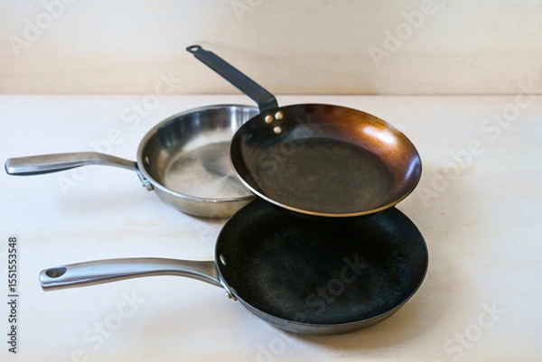 Fototapeta Three frying pans without unhealthy non-stick coating made of carbon steel, stainless steel and cast iron on a light wooden background, copy space, selected focus