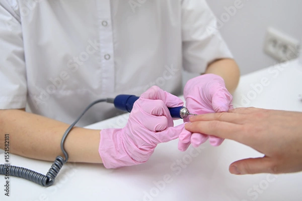 Fototapeta The manicure master performs a hardware manicure for the client in pink latex gloves, ensuring careful nail care so that they look flawless. Close-up of women's hands, hardware manicure