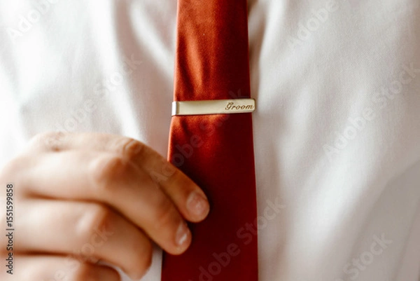 Obraz Elegant man putting tie bar on red tie