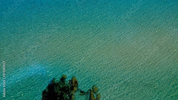 Fototapeta Clear Turquoise Water Gently Ripples in a Serene Coastal Setting With Rocky Edges Under Bright Sunlight