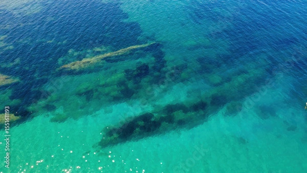 Fototapeta Clear Turquoise Waters Reveal Submerged Rocks and Marine Life Near a Coastal Area During a Sunny Afternoon