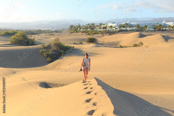 Fototapeta A traveler strides across golden sand dunes in Fuerteventura, enjoying the sunlight and serene landscape in the Canary Islands.