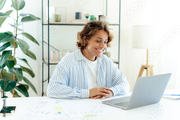 Obraz Happy confident brazilian woman smiling and listening colleagues during a virtual meeting. Businesswoman engaged in online conversation, talking with clients with interest and positivity