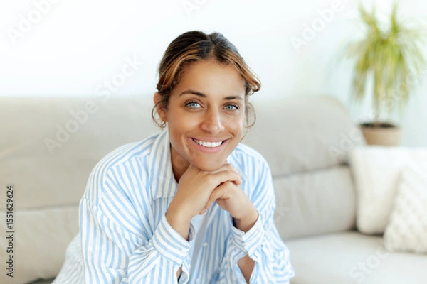 Obraz Happy pretty brazilian blue-eyed woman smiling warmly while sitting comfortably at home. Relaxed and confident, she looks directly at camera, expressing calm and friendly mood in a casual moment