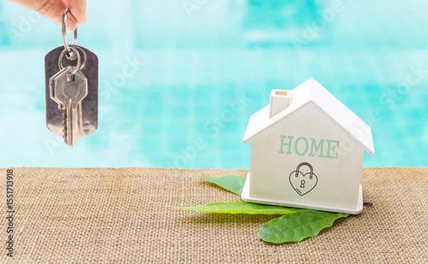 Obraz House key in girl hand with wooden house model on swimming pool edge, Green house, environmental concept, eco house