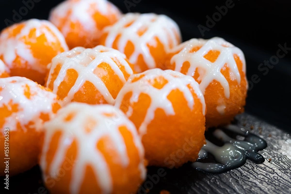 Fototapeta Sushi balls covered in bright orange tobiko and drizzled with white mayonnaise on a black tray, highlighting texture and vibrant color.
