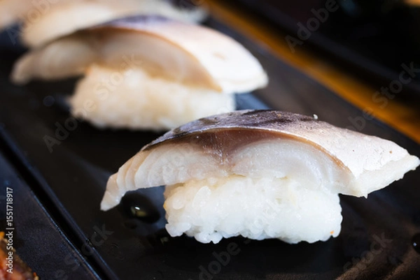 Fototapeta Saba nigiri sushi with a slice of grilled mackerel on top of vinegared rice, served on a black plate in a Japanese restaurant.