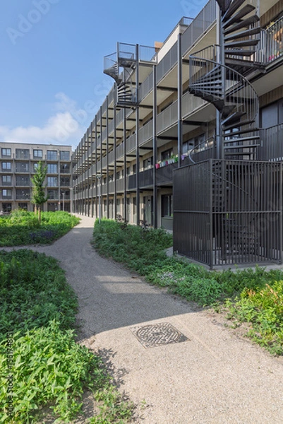 Obraz Modern modular housing in Utrecht, Netherlands, featuring multi-story temporary apartments with spiral staircases and shared green spaces, addressing urban housing shortages.