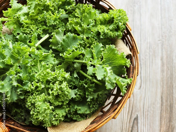 Fototapeta Top view of freshly harvested kale in a wicker basket on a rustic wooden background