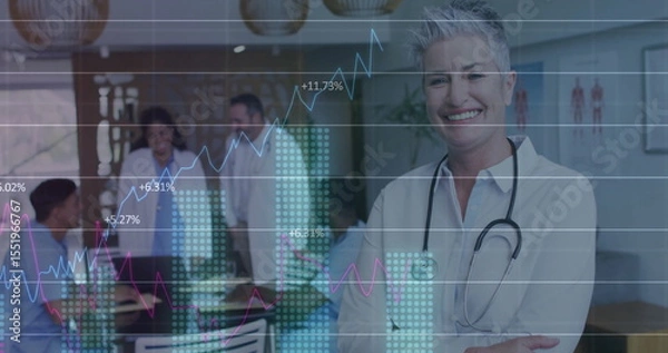 Obraz Smiling doctor in white blouse standing in clinic, with stethoscope, tablet and graph, copy space