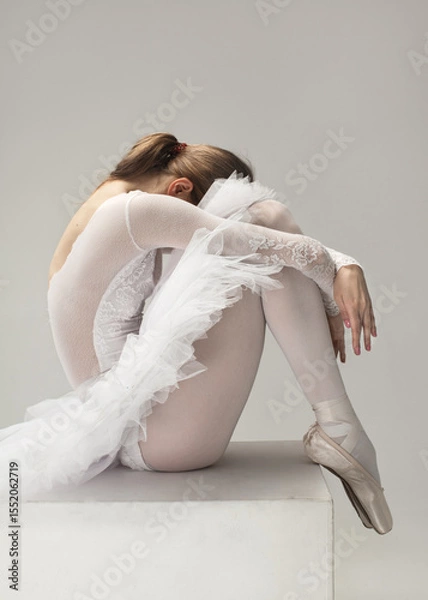 Fototapeta Graceful ballerina in white tutu resting on a pedestal, curled up in a quiet emotional pose. Minimal ballet concept.