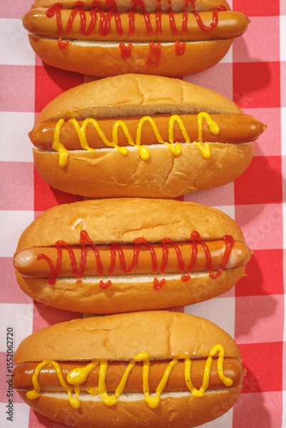 Fototapeta Close-up of four neatly arranged hot dogs with mustard and ketchup on a red checkered background. Tasty fast food concept.