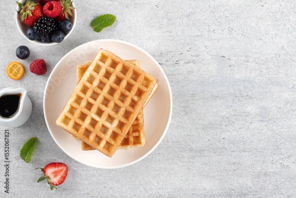 Fototapeta Plain waffles with fresh berries and maple syrup on a gray background. Copy space. Top view.