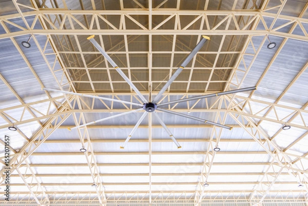 Fototapeta HVLS big fan under metal roof beam structure with heat insulation ceiling of large multipurpose building, low angle view with copy space