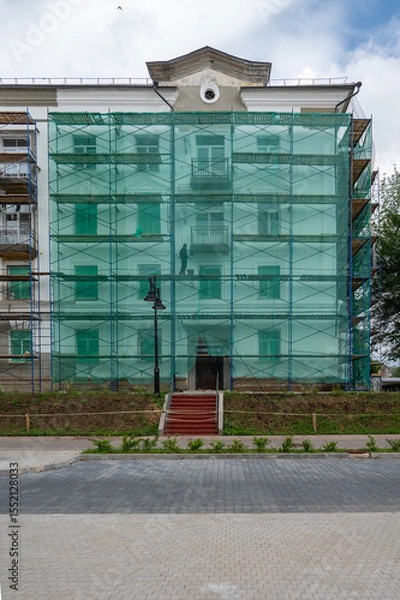 Fototapeta An old building in scaffolding during renovation and painting of the facade.